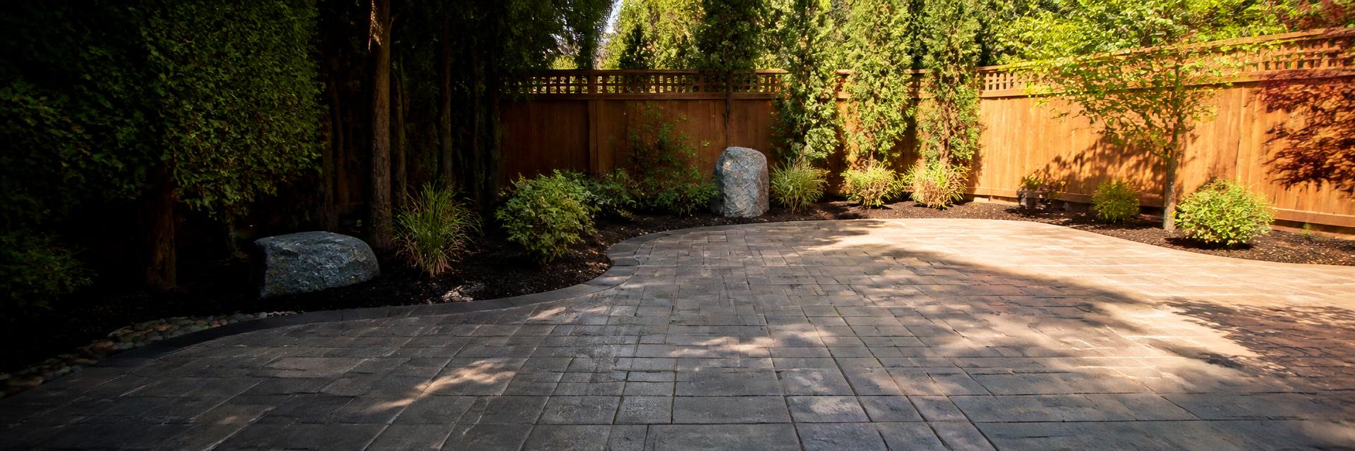 Freshly installed stone paver patio bordered by redwood fence and mulched garden beds